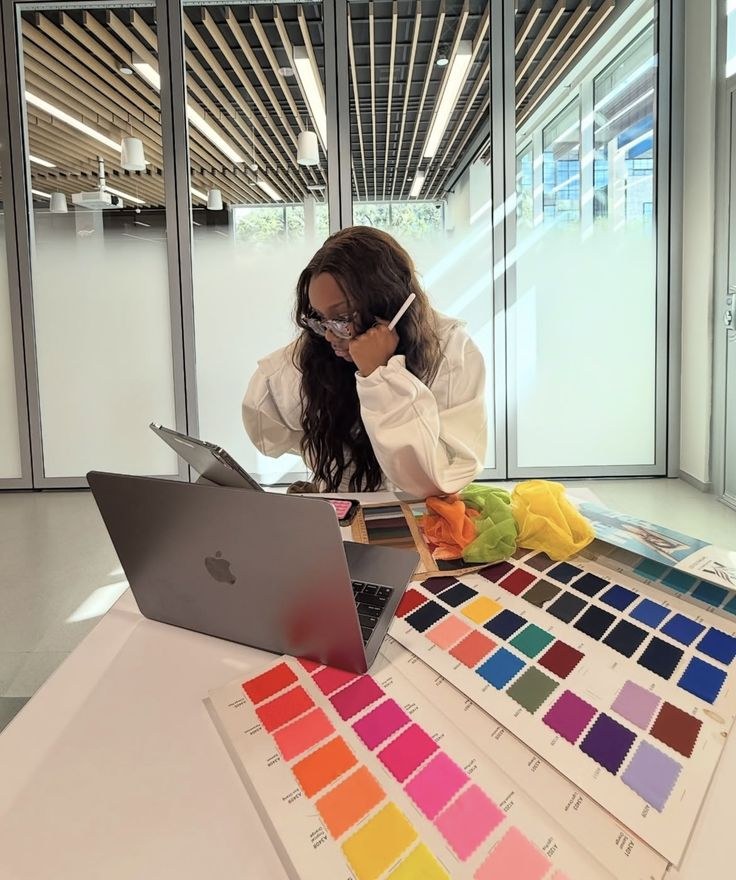 A woman with glasses working at a table covered in colourful fabric swatches