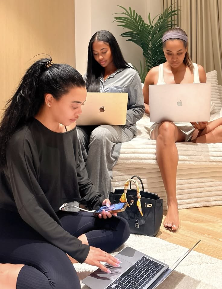 Three women working on laptops together in a warm, sunlit room